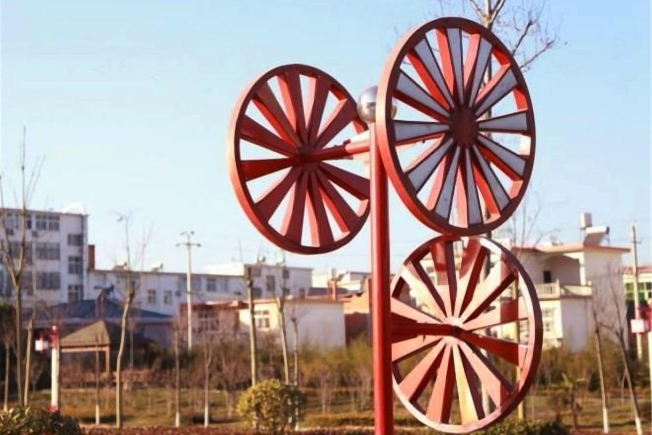 A windmill structure with a red and white color scheme, set against a residential backdrop with buildings and clear skies.