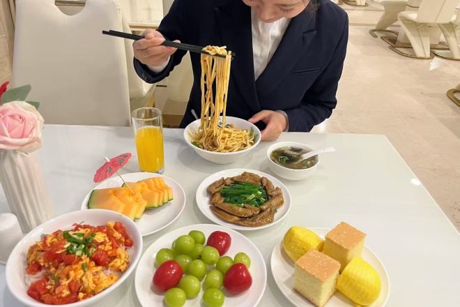 Una mesa de comedor con diferentes platos, entre ellos fideos, verduras y frutas.