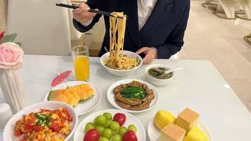 Una mesa de comedor con diferentes platos, entre ellos fideos, verduras y frutas.