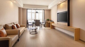 A modern living room with a sofa, a round coffee table, a TV mounted on the wall, and a dining area with chairs and a table. - Best International Hotel (Shangcheng, Xinyang) (Shangcheng)