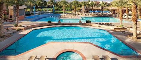 A large outdoor swimming pool with multiple sections, surrounded by palm trees and lounge chairs.
