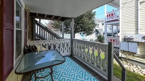 A covered porch with a glass table and patterned rug, a white railing, and a view of a neighboring house.