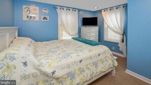 A bedroom with a bed, a dresser, a TV, and a window with curtains.