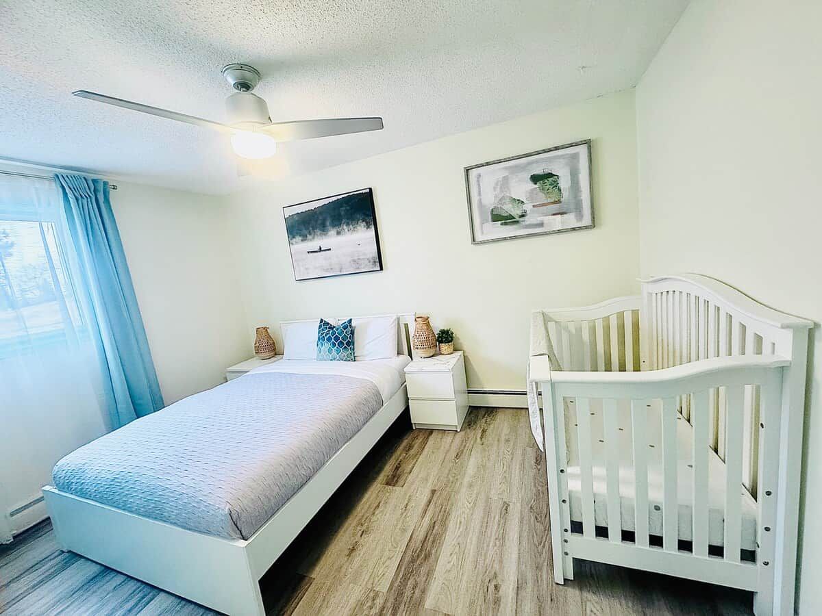 A bedroom with a bed, a crib, a nightstand, and a ceiling fan.
