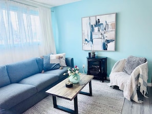 Un salon avec un canapé bleu, une table basse surmontée d’un vase, une cheminée et un tableau accroché au mur.