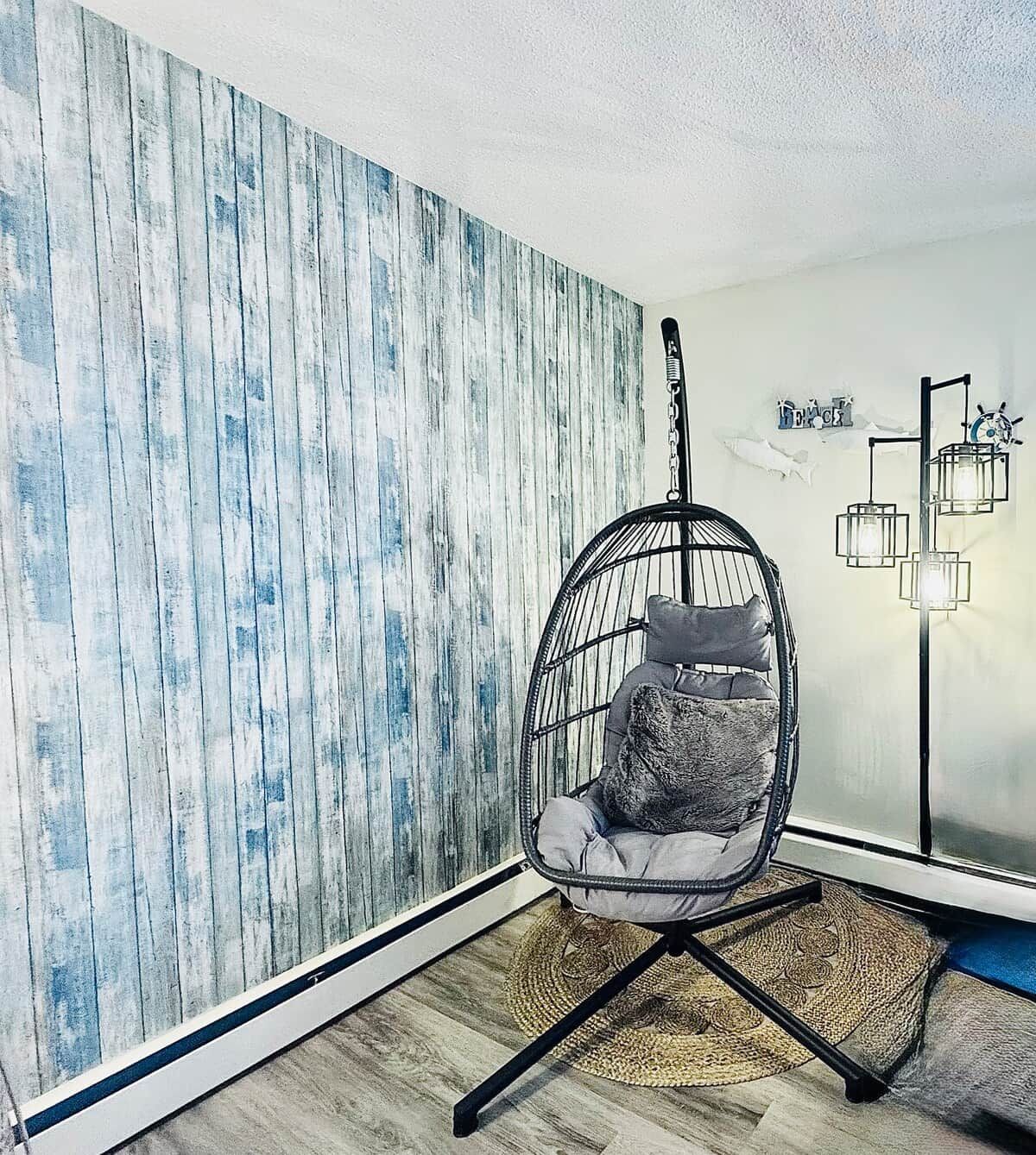 A room with a hanging chair, a patterned wall, a floor lamp, and a rug.