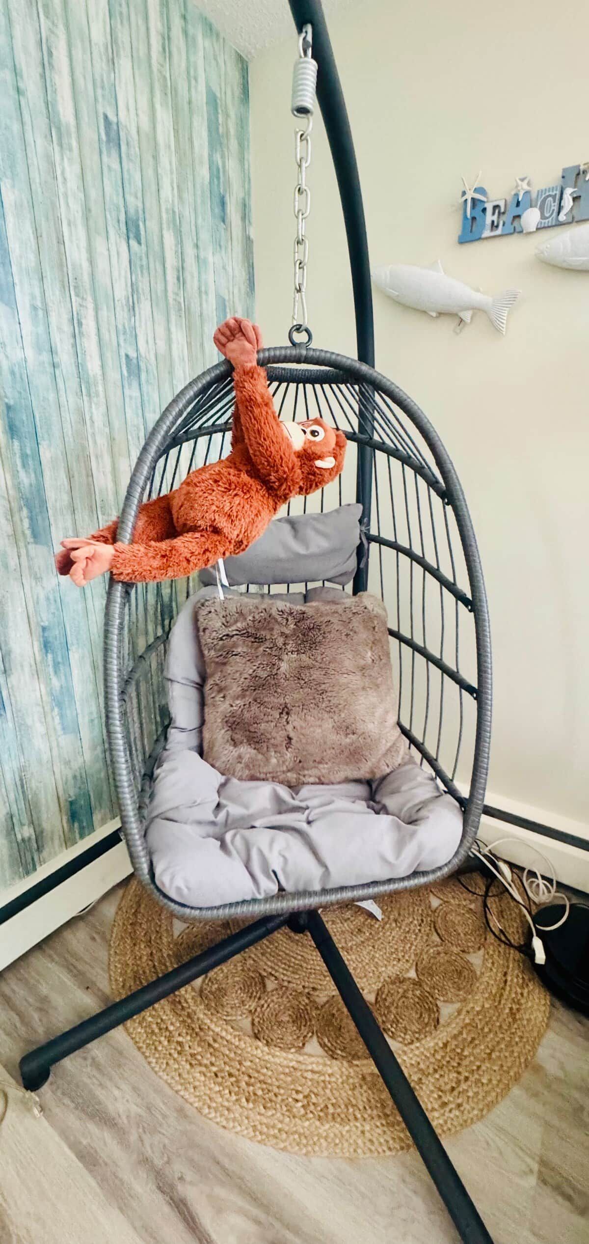 Una silla colgante con un peluche, un cojín y una pared con detalles decorativos.