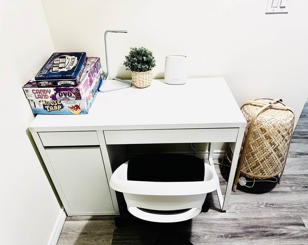 A white desk with a white chair, a small potted plant, a white mug, and a wicker bag.