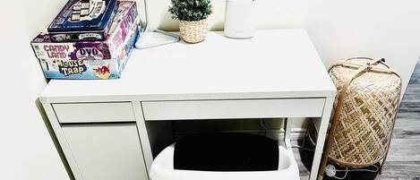 A white desk with a white chair, a small potted plant, a white mug, and a wicker bag.