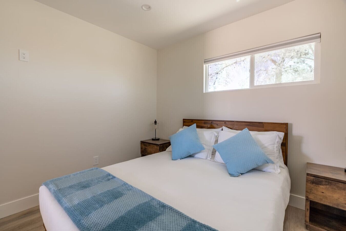 Un dormitorio con una cama, dos mesitas de noche, un ventanal y una mesita auxiliar.