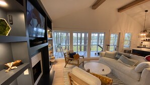 A modern living room with a fireplace, a large TV, a sofa, and a dining area with a table and chairs.