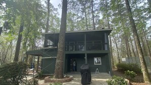 A modern two-story building with a covered outdoor seating area, surrounded by tall trees.