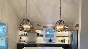 A modern kitchen with a large island, pendant lights, and stainless steel appliances.
