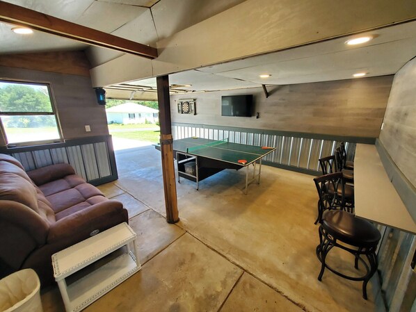 A room with a ping pong table, a couch, and a TV mounted on the wall. - Lakehouse with Game Room, Direct Water Access, and Kayaks Included! (Loogootee)