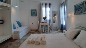 A hotel room with a bed, a small table with a vase, a chair, and a sofa. - Louis Residence (Paros)
