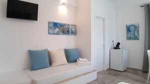 A modern living room with a sofa, a flat-screen TV, artwork, a refrigerator, and a chair. - Louis Residence (Paros)