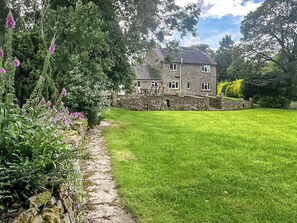 A stone house with a stone wall and a grassy lawn.