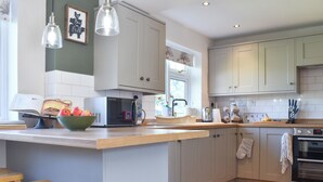 Een keuken met een centraal eiland, houten krukken, een magnetron en een spoelbak.