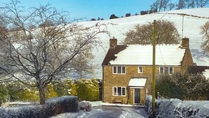 Een stenen huis met een met sneeuw bedekte dak, een verharde oprit en een stenen muur aan één kant.
