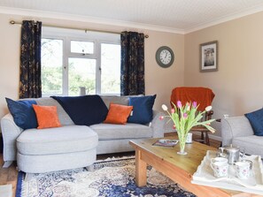A living room with a grey sofa, a coffee table, a clock, and a vase with flowers.