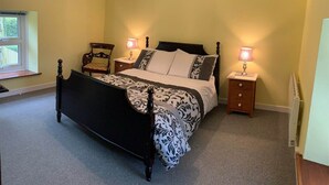 A bedroom with a large bed, two bedside tables with lamps, a window, and a radiator.