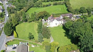 An aerial view of a large estate with expansive green lawns, a main house, and several smaller buildings.