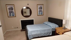 Een hotelkamer met een bed, nachtkastje, lamp, open haard en twee ingelijste foto’s aan de muur.