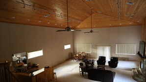 Een ruime woonkamer met hoge plafonds, houten balken, een open haard en een eethoek met stoelen en een tafel.