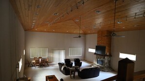 Een ruime woonkamer met houten plafond, open haard, televisie en een eethoek.