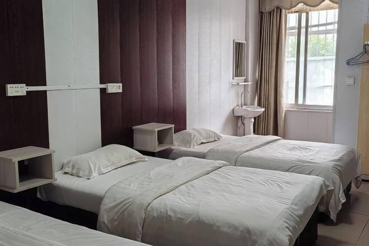 Habitación de hotel con dos camas, una mesita de noche, un armario pequeño, un espejo y una ventana con cortinas.