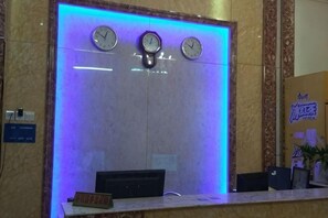 A reception desk with clocks, a marble wall, and a blue light. - Bandung Hotel (Wuzhou)