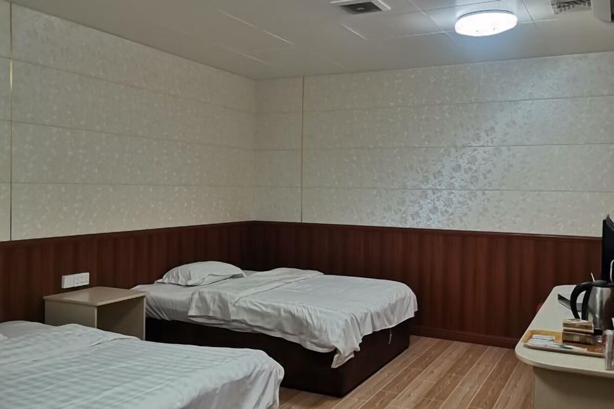 Habitación de hotel con dos camas, cabecera de madera, un escritorio con una silla y una mesita de noche pequeña.