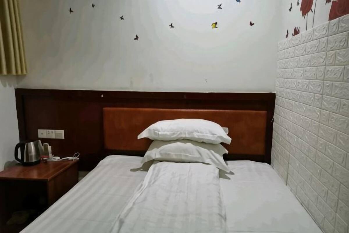 Habitación de hotel con cama, mesita de noche, hervidor y una pared decorada con un adhesivo de pájaro.
