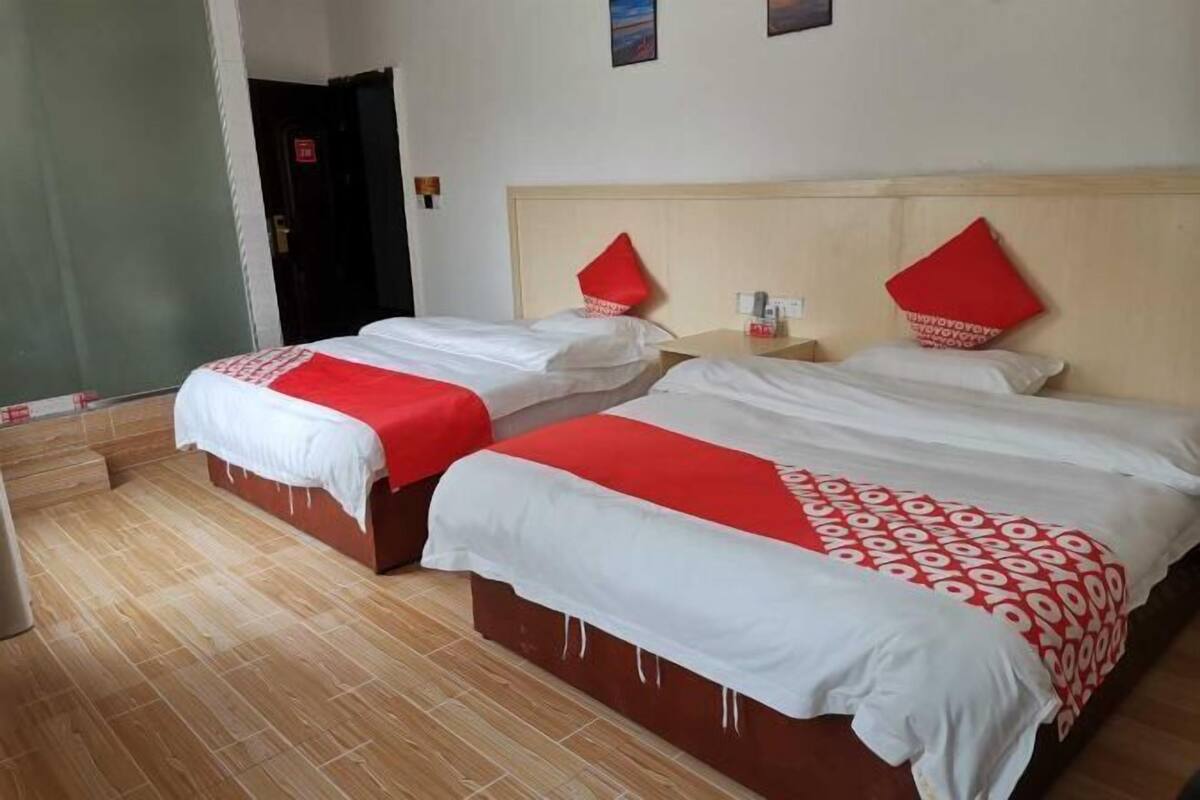 Habitación de hotel con dos camas, cada una con una colcha estampada en rojo y blanco, un cabecero de madera y una mesita de noche con una lámpara.