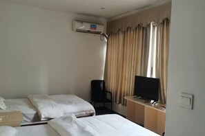 Habitación de hotel con dos camas, un escritorio con televisor, una silla y un equipo de aire acondicionado.
