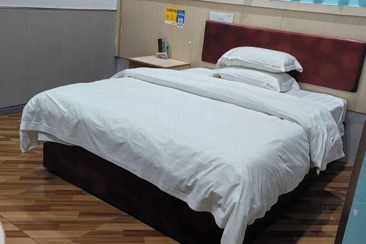 Habitación de hotel con cama, mesita de noche, cabecera roja y suelo de madera.