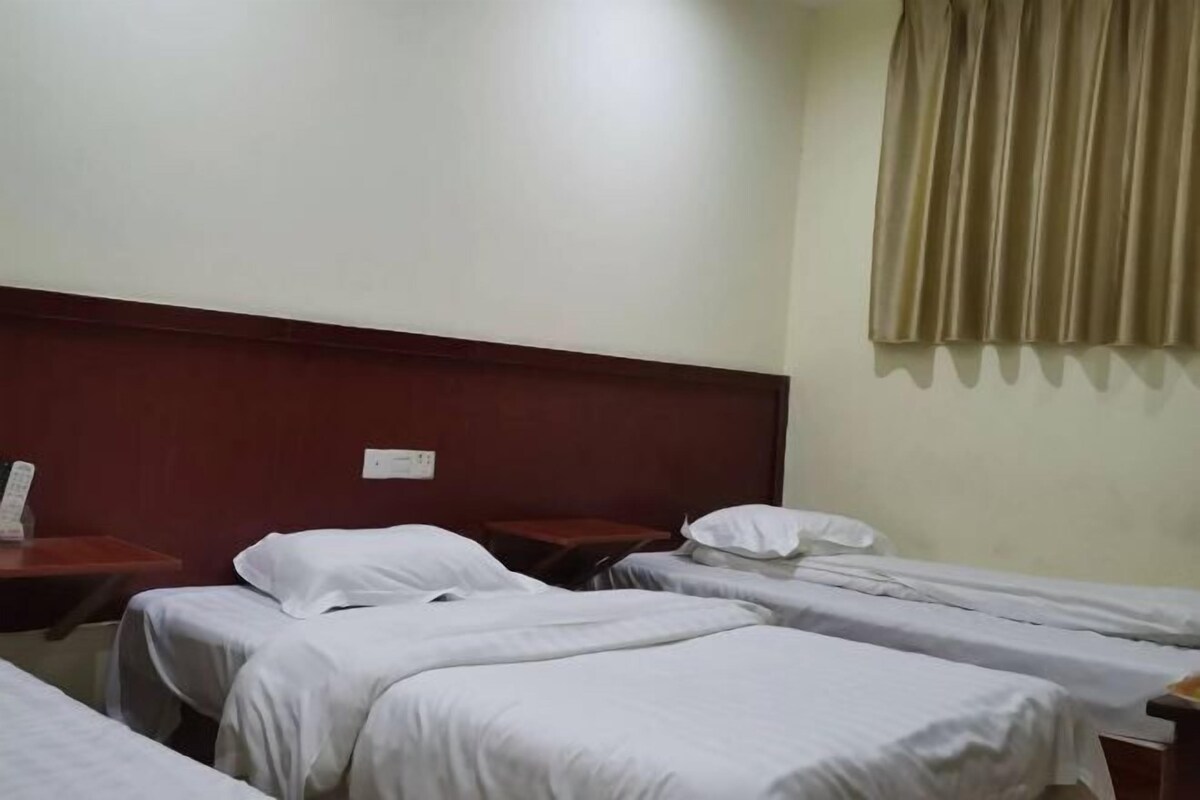Habitación de hotel con tres camas individuales, cabecera de madera, mesita de noche con teléfono y ventana con cortinas.