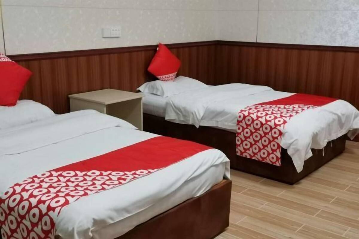 Habitación de hotel con dos camas, cada una con una colcha roja y blanca. Hay una mesita de noche pequeña entre las camas.