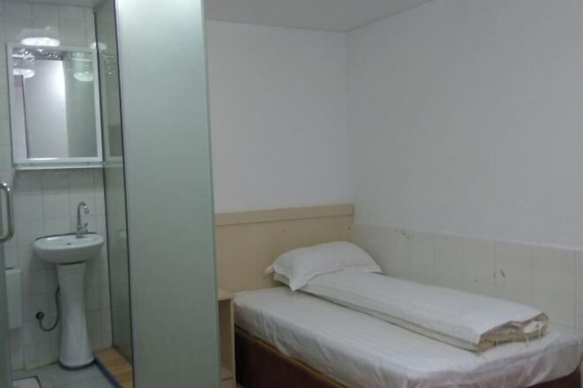 Una habitación pequeña con cama individual, una mesita de noche, un lavabo blanco y un espejo.