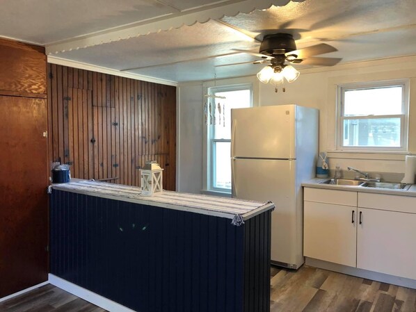 A kitchen with a wooden accent wall, a white refrigerator, a sink, and a ceiling fan.