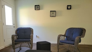Una habitación con dos mecedoras de mimbre, un otoman negro y una puerta.