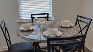 Una mesa de comedor redonda con platos blancos, tazones y cristalería transparente, rodeada de sillas negras.
