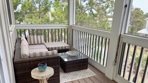 A covered porch with a wicker sofa, striped cushions, a glass coffee table, and a small round table with a bowl. - Perfect beach getaway! Bike to beach, pool - 4 cruisers included! (Rosemary Beach)