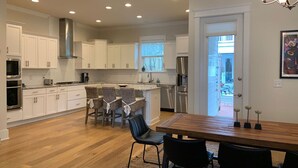 A modern kitchen with white cabinets, stainless steel appliances, a dining area with a wooden table and chairs, and a view of the backyard through a door. - Perfect beach getaway! Bike to beach, pool - 4 cruisers included! (Rosemary Beach)