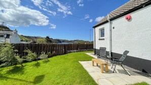 A backyard with a white house, a wooden fence, a bench, and a table. - Cute, comfy bolthole in an amazing spot to explore from. (Kinlochbervie, near Lochinver)