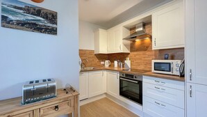 A modern kitchen with white cabinets, a wooden countertop, a built-in oven, a microwave, and a toaster. - Cute, comfy bolthole in an amazing spot to explore from. (Kinlochbervie, near Lochinver)