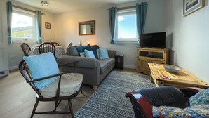 A cozy living room with a sofa, armchairs, a coffee table, and a television. - Cute, comfy bolthole in an amazing spot to explore from. (Kinlochbervie, near Lochinver)