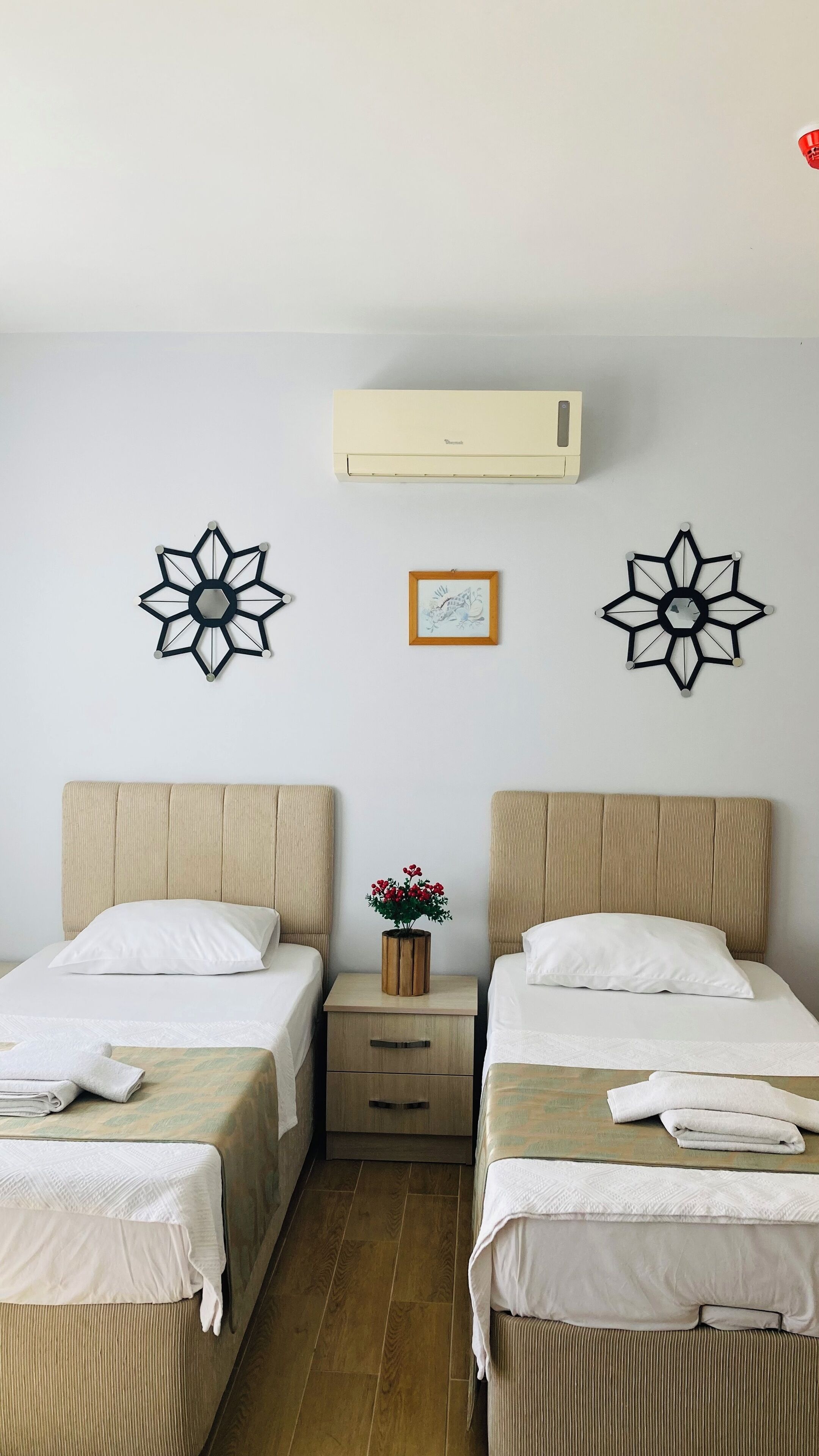 Een hotelkamer met twee bedden, een nachtkastje, een wandairconditioner en decoratieve muurkunst.