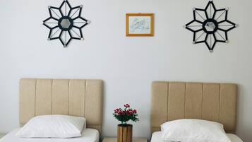 Een hotelkamer met twee bedden, een nachtkastje, een wandairconditioner en decoratieve muurkunst.