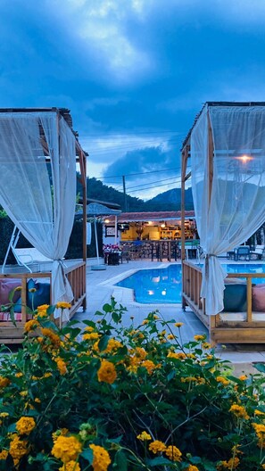 A poolside area with a bar and outdoor seating, surrounded by a wooden pergola with white curtains. - Bybassios Hotel (Marmaris)